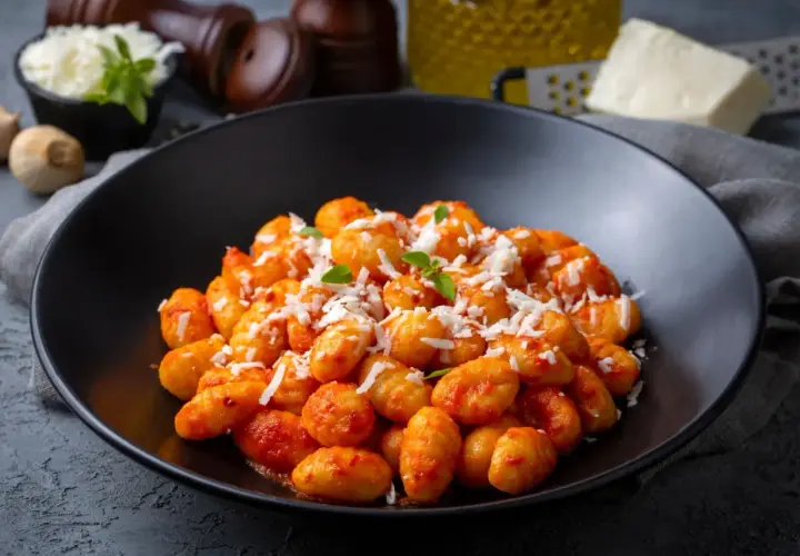 Gnocchi di ceci e patate conditi con sugo rosso e parmigiano grattugiato, guarniti con basilico fresco.