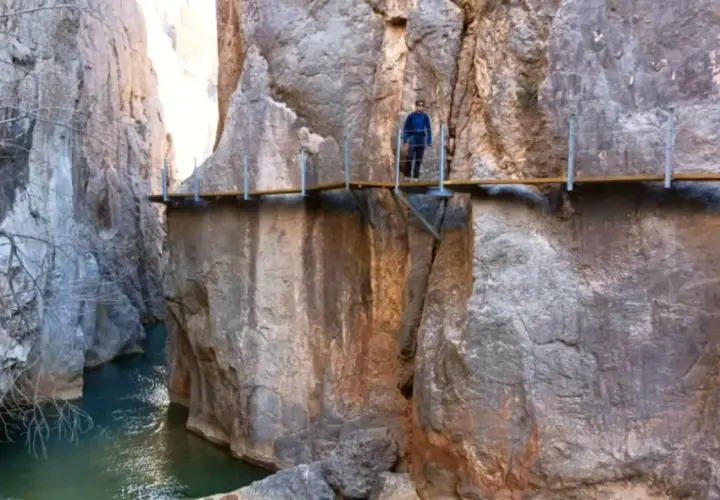 Un excursionista camina por las pasarelas de Valloré, un sendero suspendido sobre un río turquesa entre imponentes paredes rocosas.