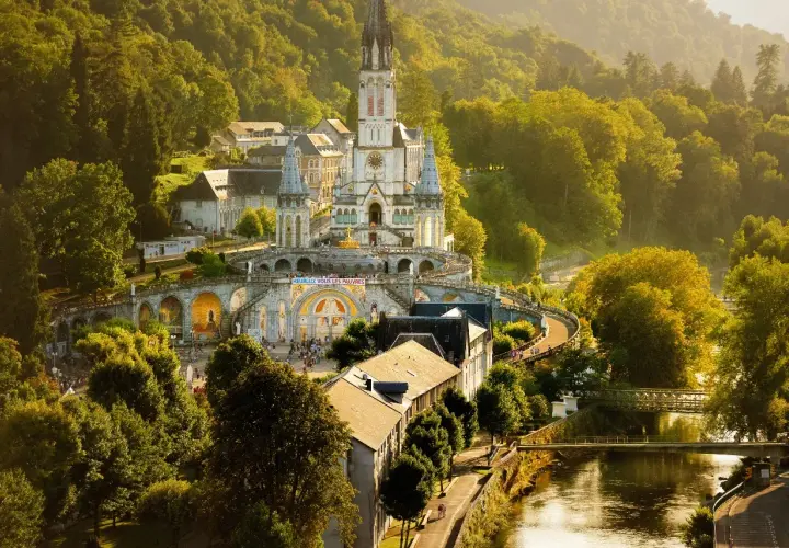 Bazylika w Lourdes, francuskie ośrodek kultu maryjnego, w otoczeniu zielonych wzgórz i rzeki.