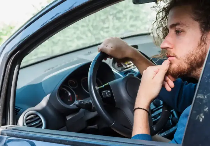 Hombre con barba y pelo rizado, pensativo, con la mano en la barbilla, mientras gira el volante y escucha un **ruido clack clack al girar el volante en parado**.