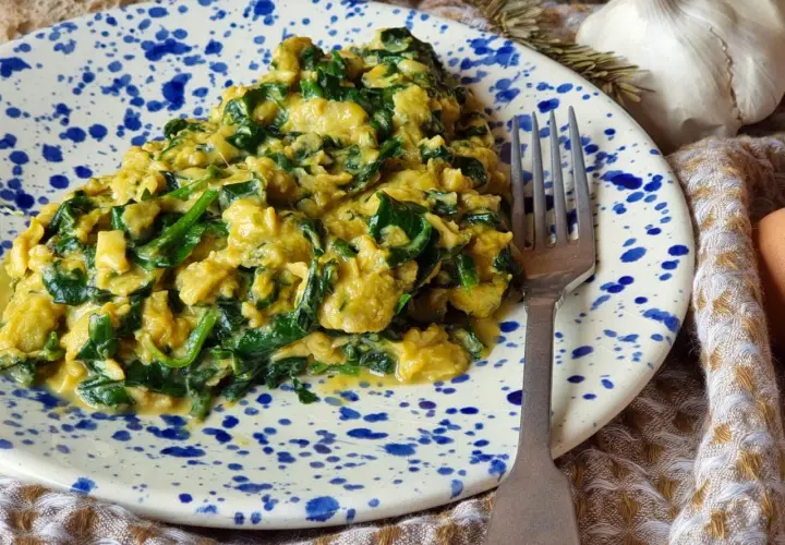 Delicioso revuelto de espinacas cremoso y sabroso, servido en un plato con salpicaduras azules. Un tenedor plateado descansa a su lado.