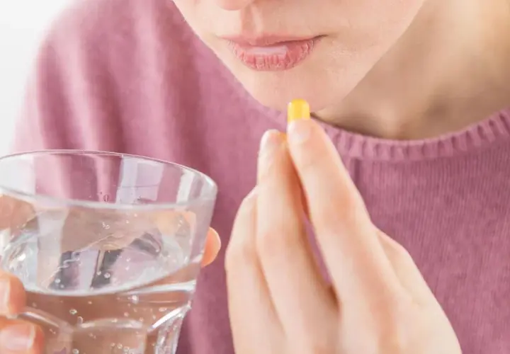 Frau nimmt Kapsel mit Wasser ein, hofft auf Linderung von Tinnitus durch Ashwagandha.