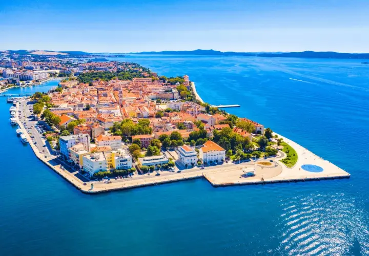 Widok z lotu ptaka na zabytkowe miasto Zadar z czerwonymi dachami, otoczone błękitnym morzem.