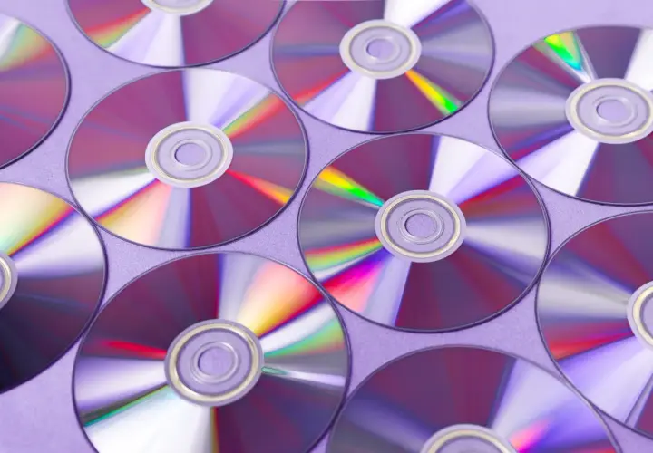 Płyty CD ułożone na fioletowym tle, odbijające światło.
