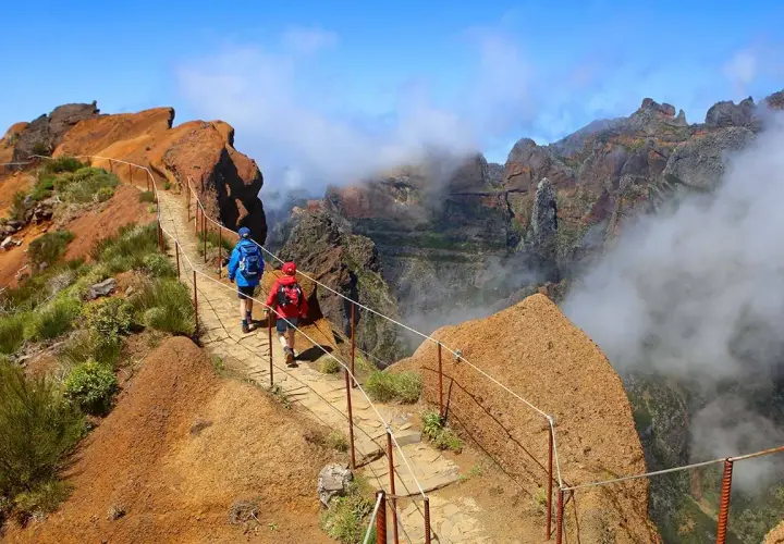 Hikers on a mountain path, a perfect example of things to do in Madeira. Dramatic cliffs and clouds surround them.