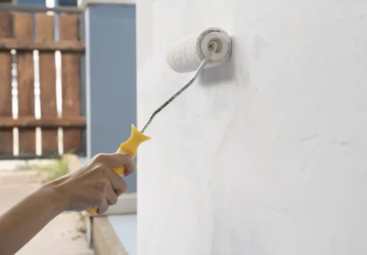 Mano aplica imprimación blanca a una pared con un rodillo. Se puede dar imprimación encima de pintura para un mejor acabado.