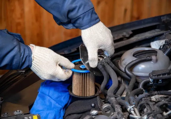 Ręce w rękawiczkach dokonują wymiany filtra paliwa diesel. Nowy element jest gotowy do montażu.
