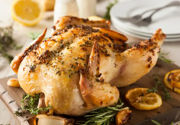 Un délicieux poulet à la broche, doré et savoureux, garni d'herbes fraîches et de quartiers de citron grillés sur une planche en bois.