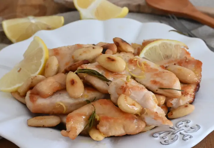 Succulento pollo al limone con mandorle tostate e rosmarino, guarnito con spicchi di limone fresco.