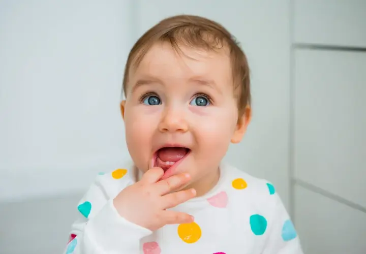 Bambino con dentizione neonato sintomi, che si porta il dito alla bocca con un'espressione curiosa.