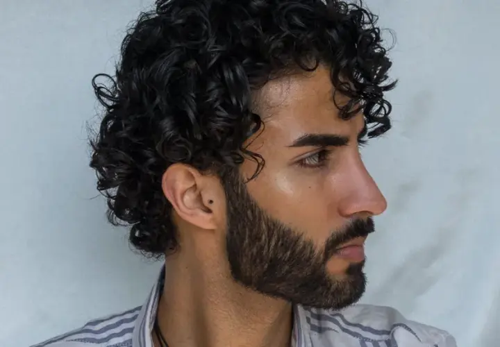 Perfil de hombre con pelo ondulado oscuro y barba cuidada.