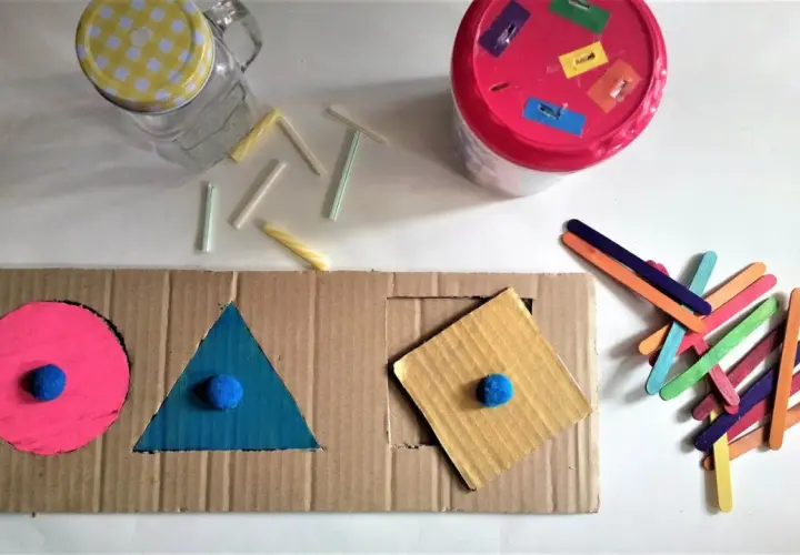 Kolorowe zabawki DIY dla niemowlaka: sorter kształtów z kartonu, patyczki i słoik.