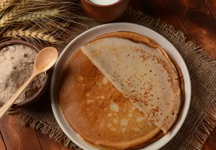 Crêpes dorées faites avec de la farine semi-complète, prêtes à être dégustées. À côté, un bol de farine et des épis de blé.