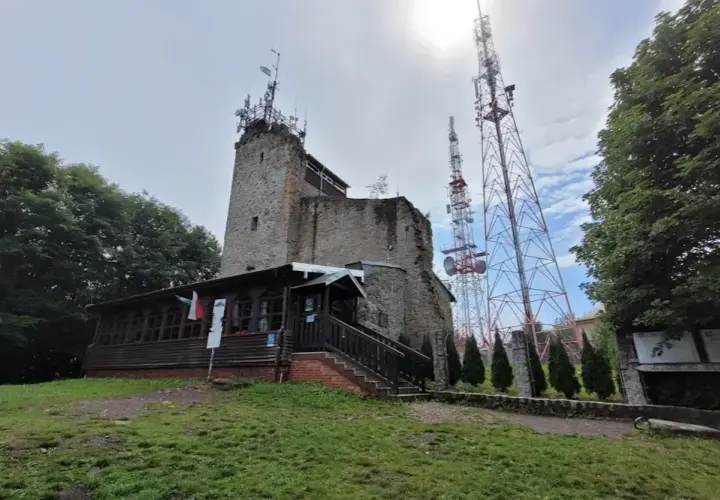 Kamienna wieża i drewniana przybudówka na szczycie góry. W tle wysokie maszty telekomunikacyjne. To popularne miejsce na szlaki turystyczne, jak Chełmiec.
