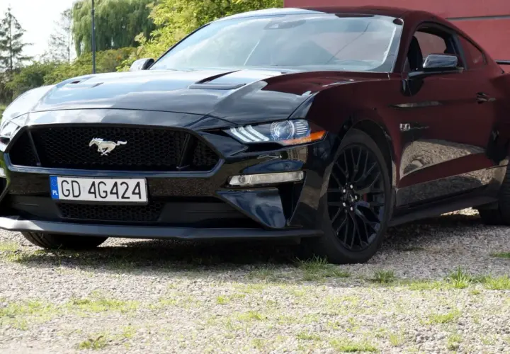 Czarny Ford Mustang z polską tablicą rejestracyjną stoi na żwirowej nawierzchni.