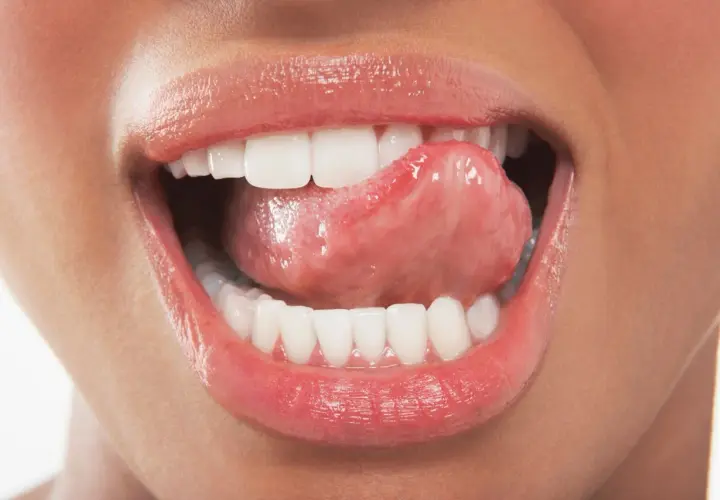 Labbra lucide e lingua che accarezza i denti ruvidi, un gesto sensuale che invita a scoprire.