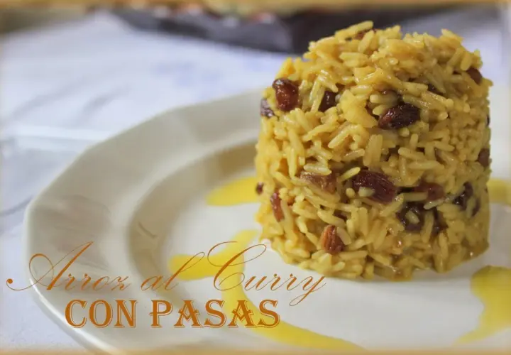 Arroz al curry con pasas, un plato aromático y dulce servido en un plato blanco con un toque de salsa dorada.