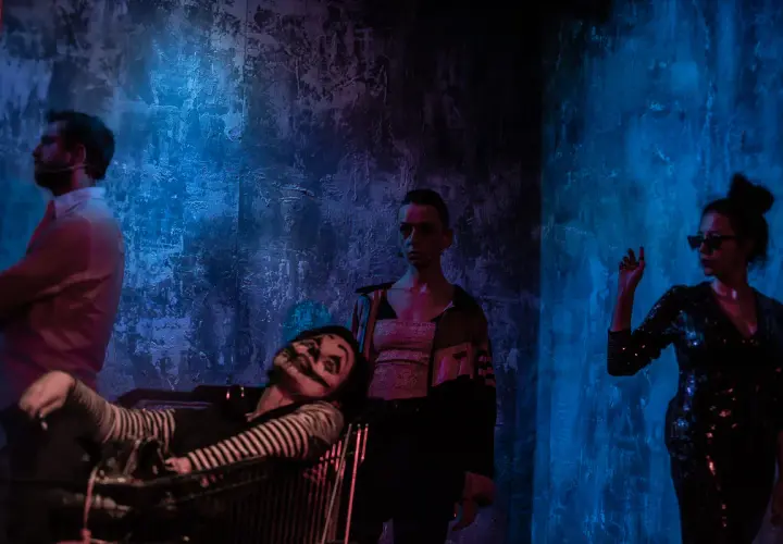 Scena z teatru Barakah. Aktor w wózku, klaun z makijażem, kobieta w cekinowej sukience i mężczyzna w białej koszuli.