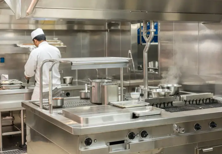 Un chef travaille dans une cuisine professionnelle étincelante, tout en acier inoxydable, le meilleur inox pour une hygiène parfaite.
