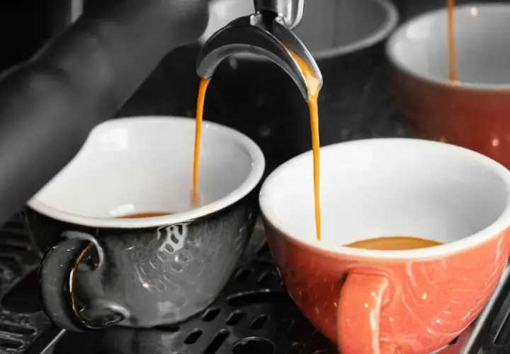 Dwa kubki, jeden czarny, drugi czerwony, napełniane są gorącym, aromatycznym espresso doppio.