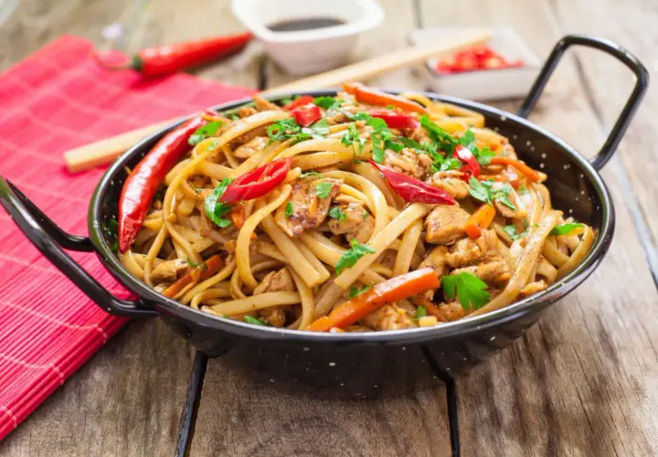 Pyszny makaron chow mein z kurczakiem, papryką i chili, posypany świeżą pietruszką.