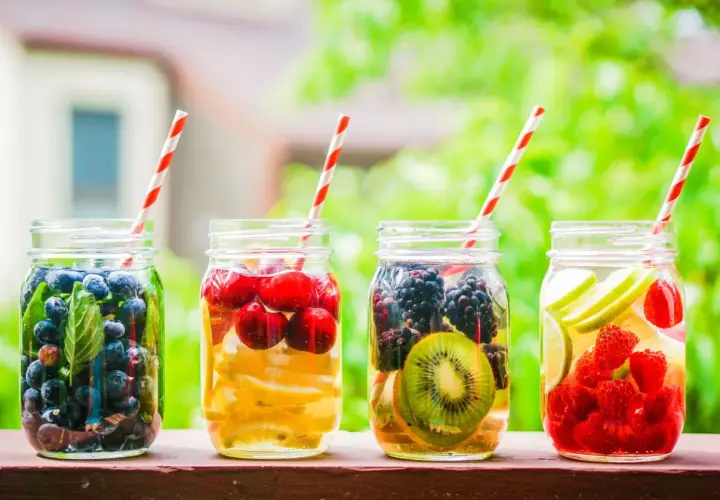 Quattro barattoli con acqua detox: mirtilli, ciliegie e limone, more e kiwi, lamponi e lime.