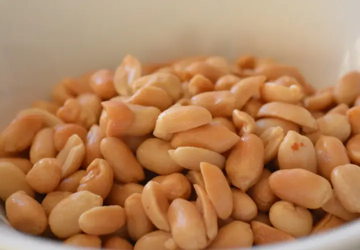 Un cuenco blanco lleno de cacahuetes o maní tostados, listos para ser disfrutados como un snack saludable.