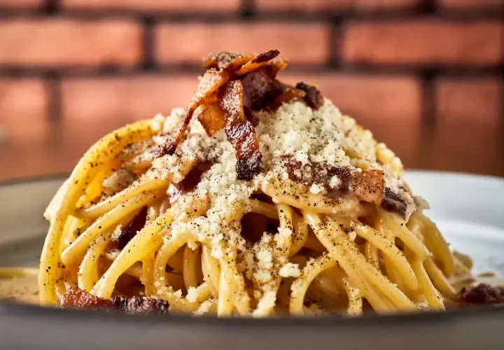 Pyszny makaron włoski carbonara, posypany parmezanem i chrupiącym boczkiem, na tle ceglanej ściany.