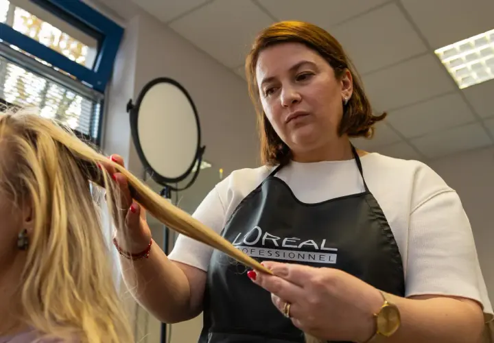 Fryzjerka w fartuchu L'Oréal Professionnel wykonuje podcinanie końcówek blond włosów.