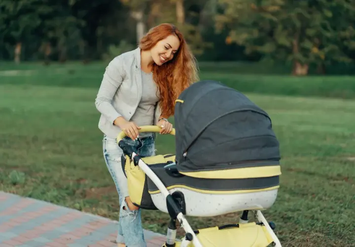 Uśmiechnięta mama z rudymi włosami pcha wózek. Idealny spacer, gdy jest 21 stopni, jak ubrać dziecko?