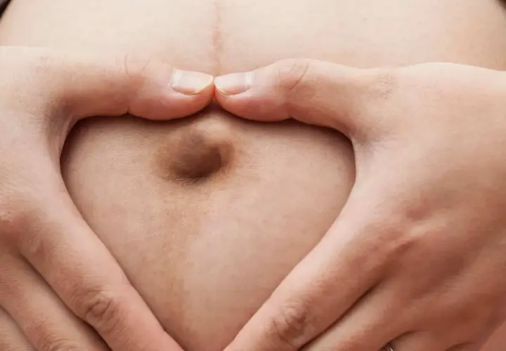 Mani a cuore circondano un ombelico in gravidanza, simbolo di amore e attesa.