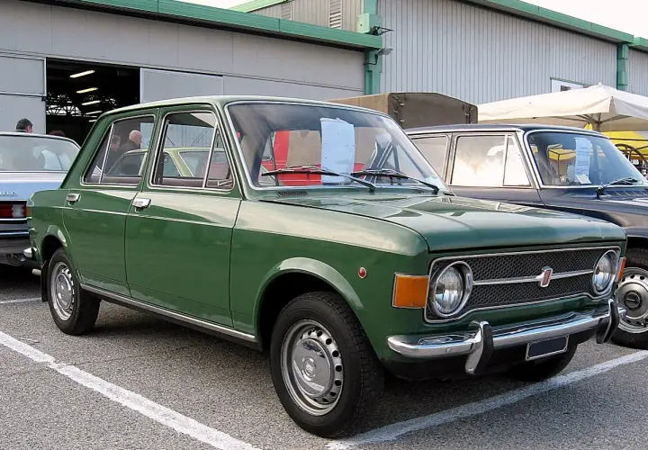 Zielony fiat 128, klasyk z lat 70., zaparkowany przed budynkiem.