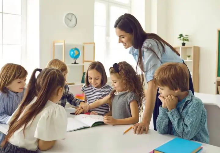 Lehrerin unterstützt Kinder bei ihrer Projektarbeit. Sie arbeiten gemeinsam an einem Buch, lernen und lachen.