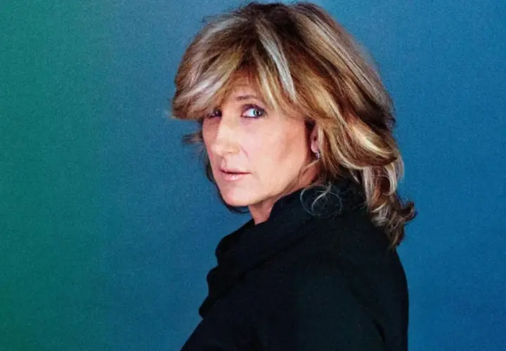 Jilliane Hoffman, mit ihrem charakteristischen blonden Haar und einem nachdenklichen Blick, posiert vor einem blauen Hintergrund.