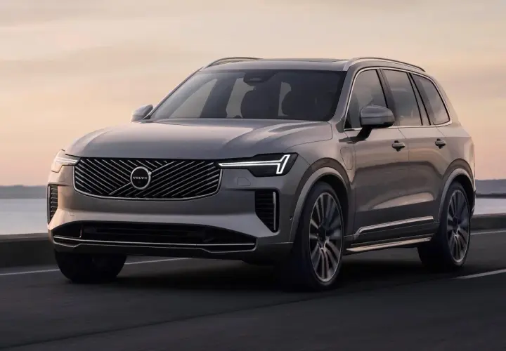 Elegancki, szary Volvo CX90 jedzie po drodze nad morzem o zachodzie słońca.