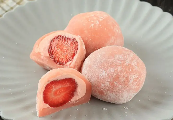Różowe mochi z truskawkami na szarym talerzu.