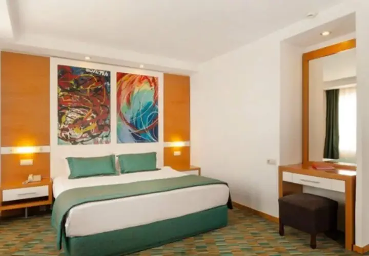 Pokój w Ladonia Hotels Adakule: łóżko z zieloną pościelą, kolorowe obrazy nad wezgłowiem, toaletka z lustrem.
