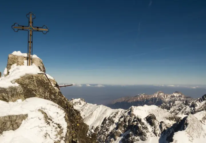 Krzyż na szczycie Gerlach, pokryty śniegiem. Widok na ośnieżone Tatry. Uważaj, by nie dostać mandatu za wejście na Gerlach bez przewodnika!