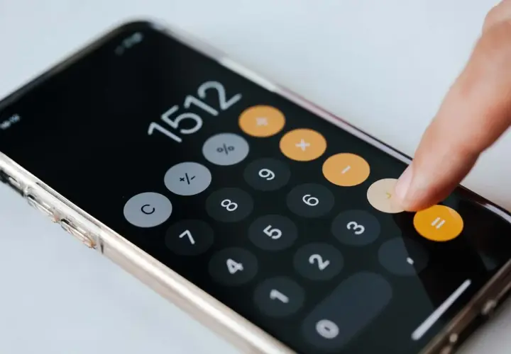 Dłoń wpisuje kwotę na kalkulatorze na smartfonie, być może obliczając przyszły próg podatkowy 2026.