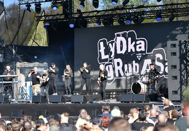 Zespół Łydka Grubasa na scenie, grający koncert. W tle wielki ekran z logo zespołu.