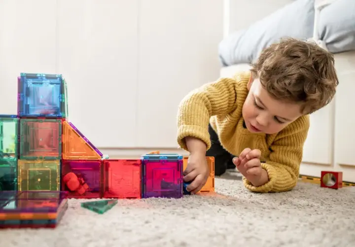 Niño concentrado jugando con bloques magnéticos de colores, ideales para actividades para niños de 2 a 3 años.