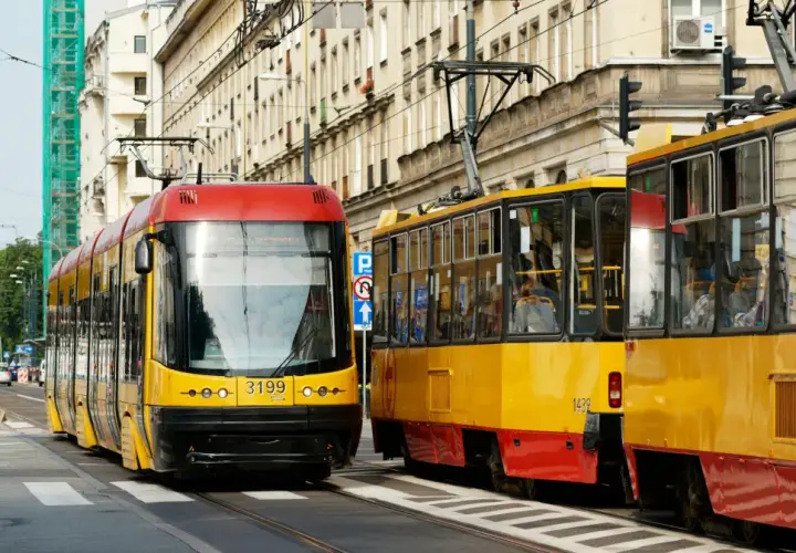 Dwa żółto-czerwone tramwaje stoją na ulicy, jeden z nich ma pierwszeństwo.