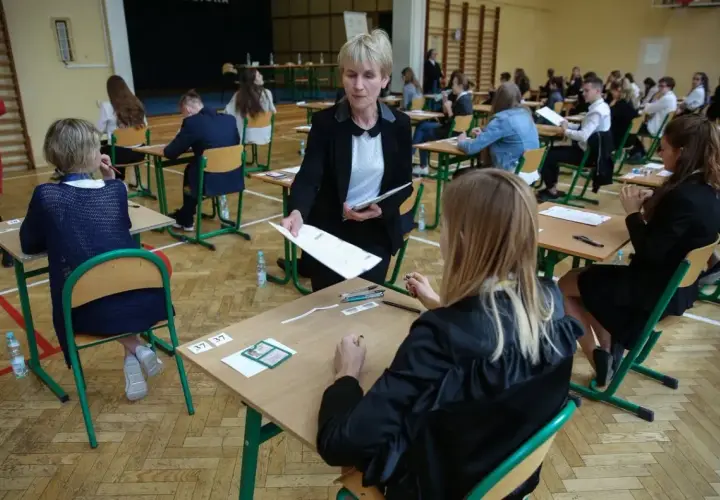 Napięcie w sali gimnastycznej, kiedy rozdawane są arkusze. Uczniowie czekają na wyniki egzaminu ósmoklasisty, a nauczycielka czuwa nad przebiegiem.