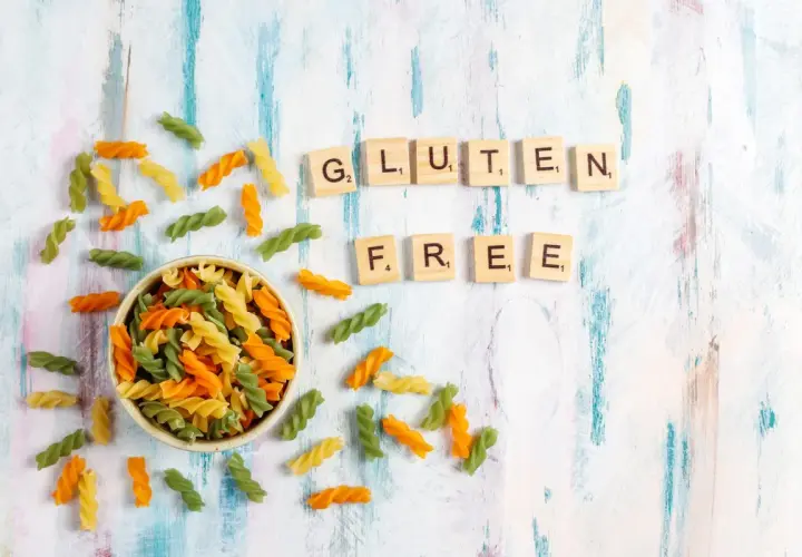 Kolorowy makaron w miseczce i rozsypane po stole, litery układające się w napis "GLUTEN FREE".