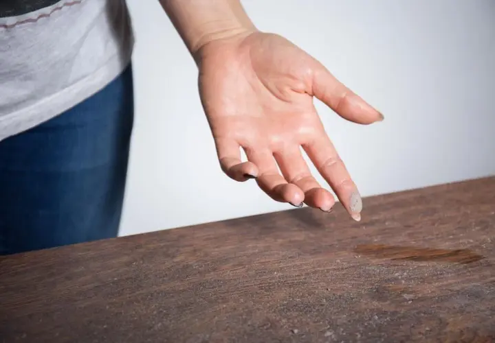Mano con polvo en los dedos sobre una mesa de madera. Una demostración visual de cómo eliminar el polvo del aire y las superficies.