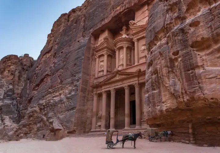 Skaliste klify Petry, Jordania, z wykutym w skale Skarbcem. Dwa wozy zaprzężone w osły czekają na turystów, marzących o jordania loty.