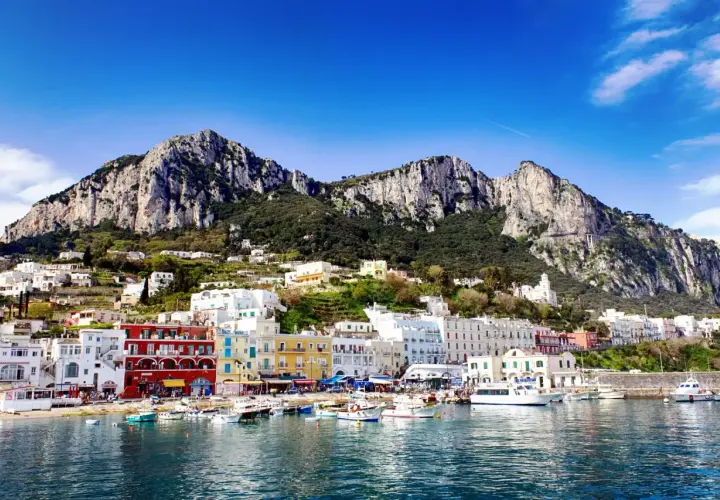 Kolorowe domy nad zatoką, góry w tle. Widok na urokliwy port na wyspie Capri.