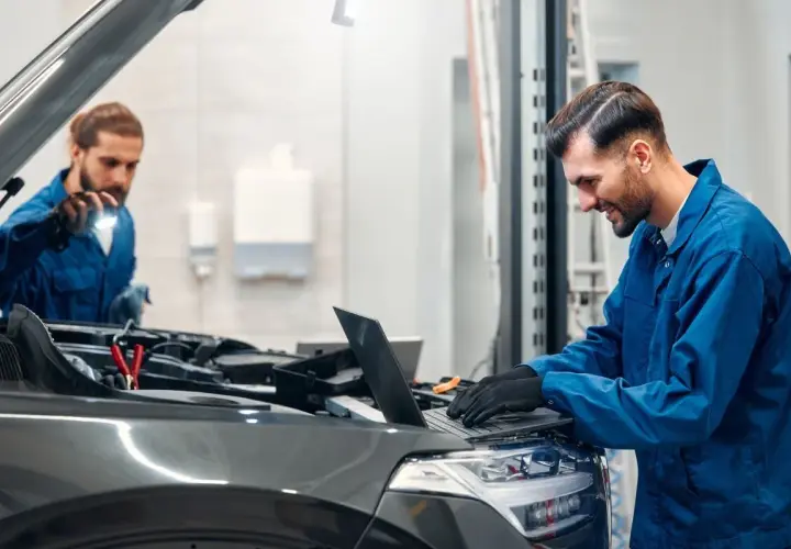 Mechanicy diagnozują drgania silnika na wolnych obrotach diesel, jeden sprawdza pod maską, drugi analizuje dane na laptopie.