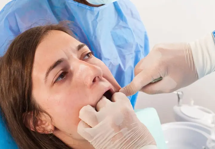 Dentista examina la boca de una paciente, notando un posible coagulo muela blanco.