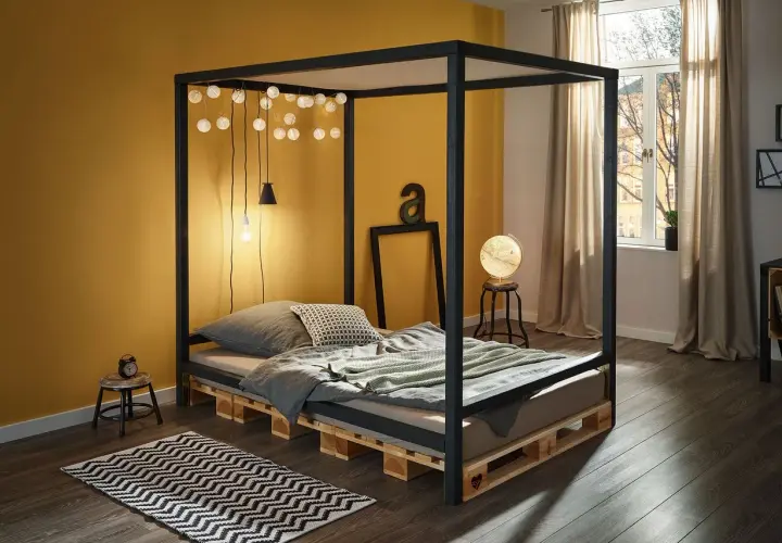 Ein modernes Himmelbett, das man leicht selber bauen kann, mit Paletten als Basis. Lichterketten und eine gelbe Wand schaffen Gemütlichkeit.